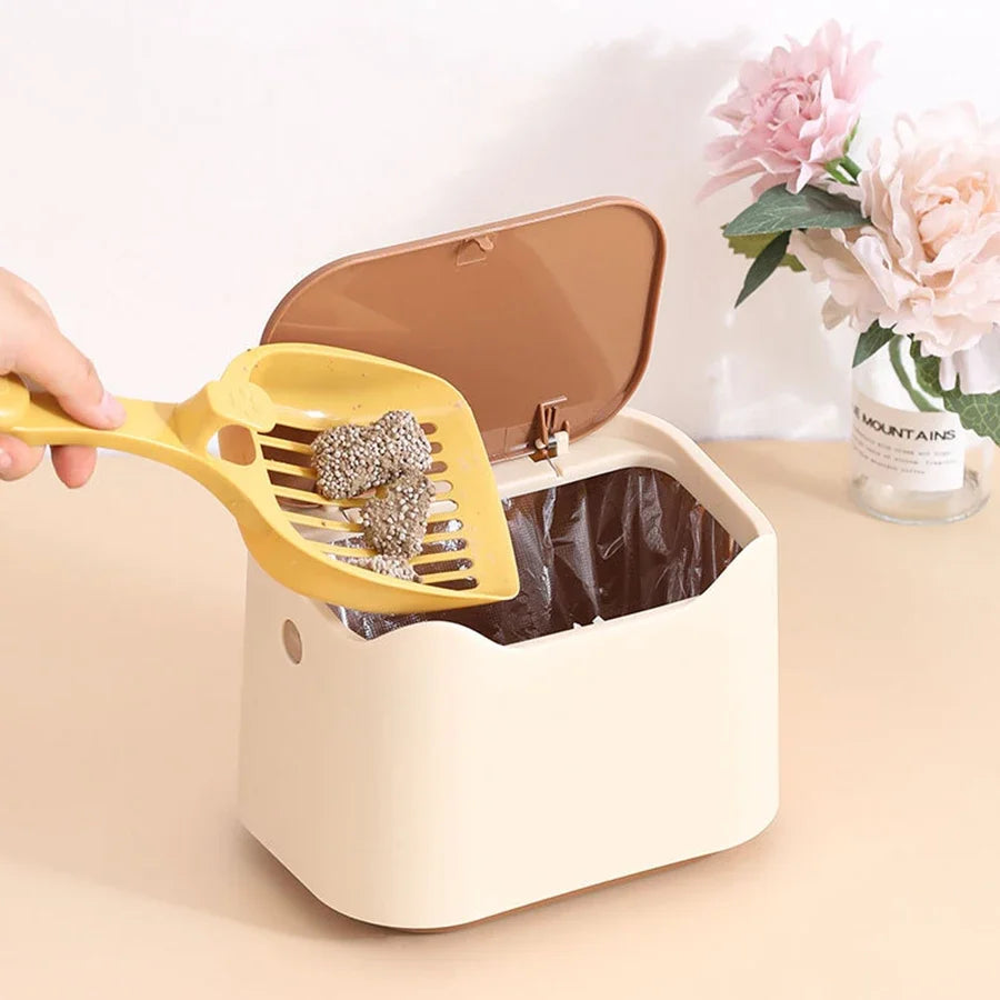 Yellow cat litter scoop being used with a beige litter box on a light surface.